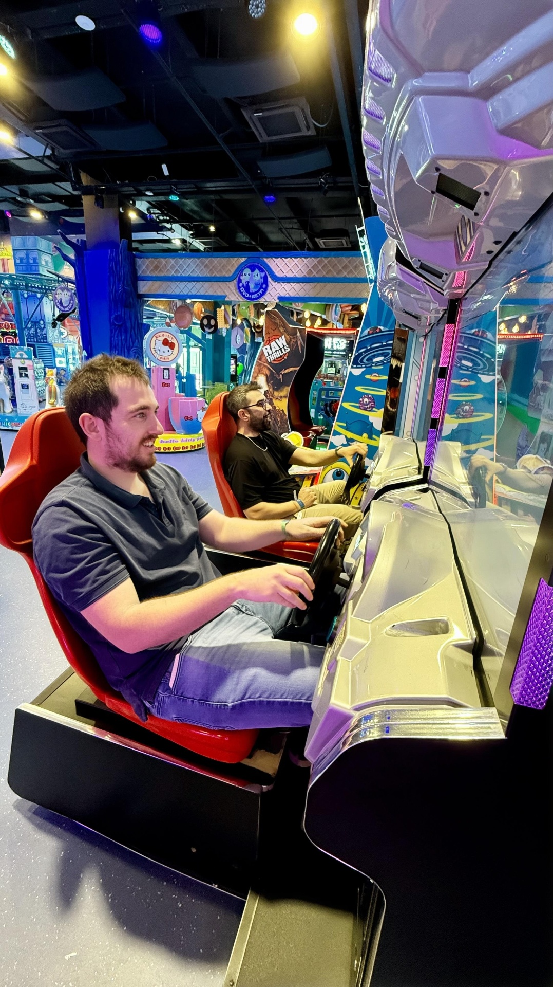 Two team members at an arcade racing cabinet